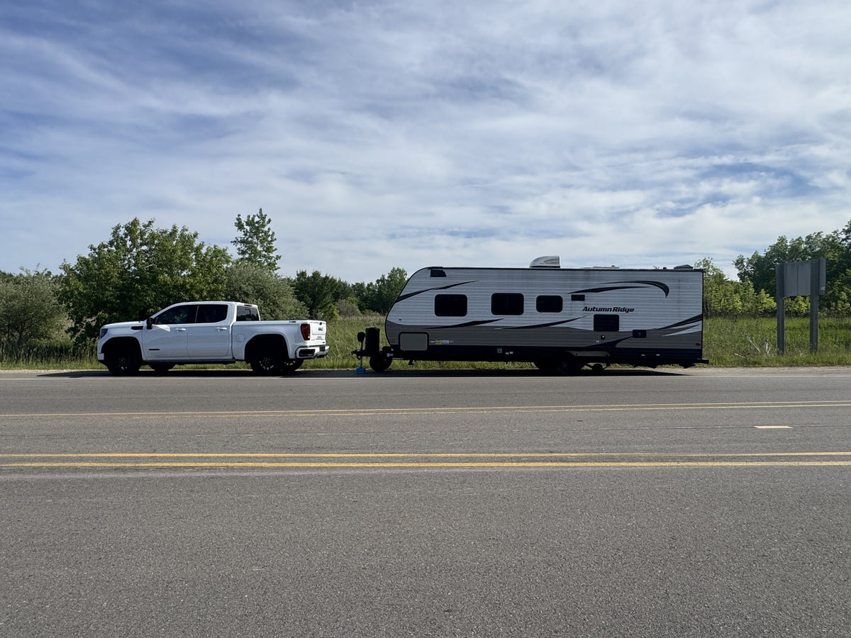 White pickup and travel trailer pulled over on the shoulder of a two-lane road